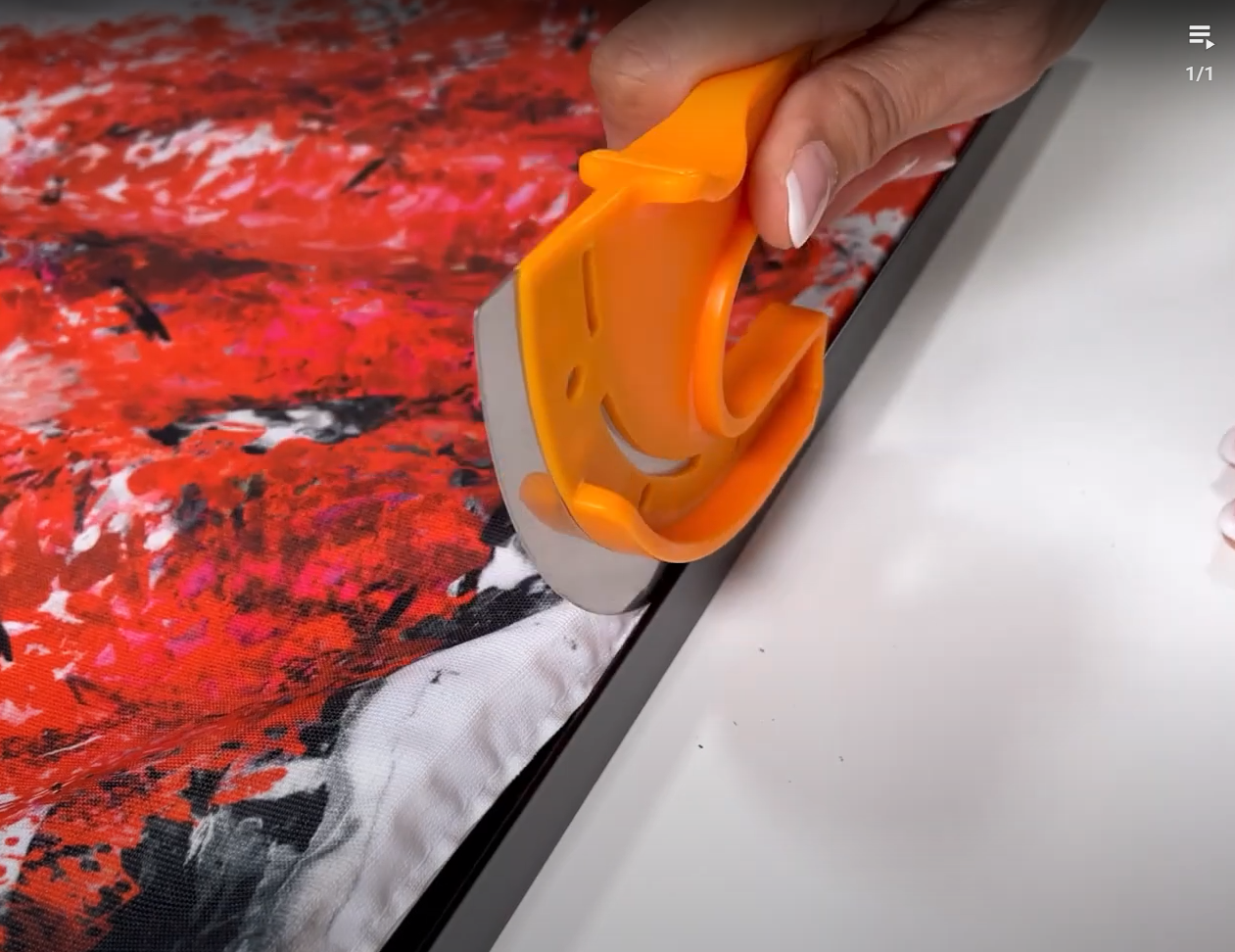 Eine Hand drückt mit dem orangenen E-Lock-Tool den Stoff mit Silikonkeder in die Nut eines schwarzen Alu-Spannrahmens
