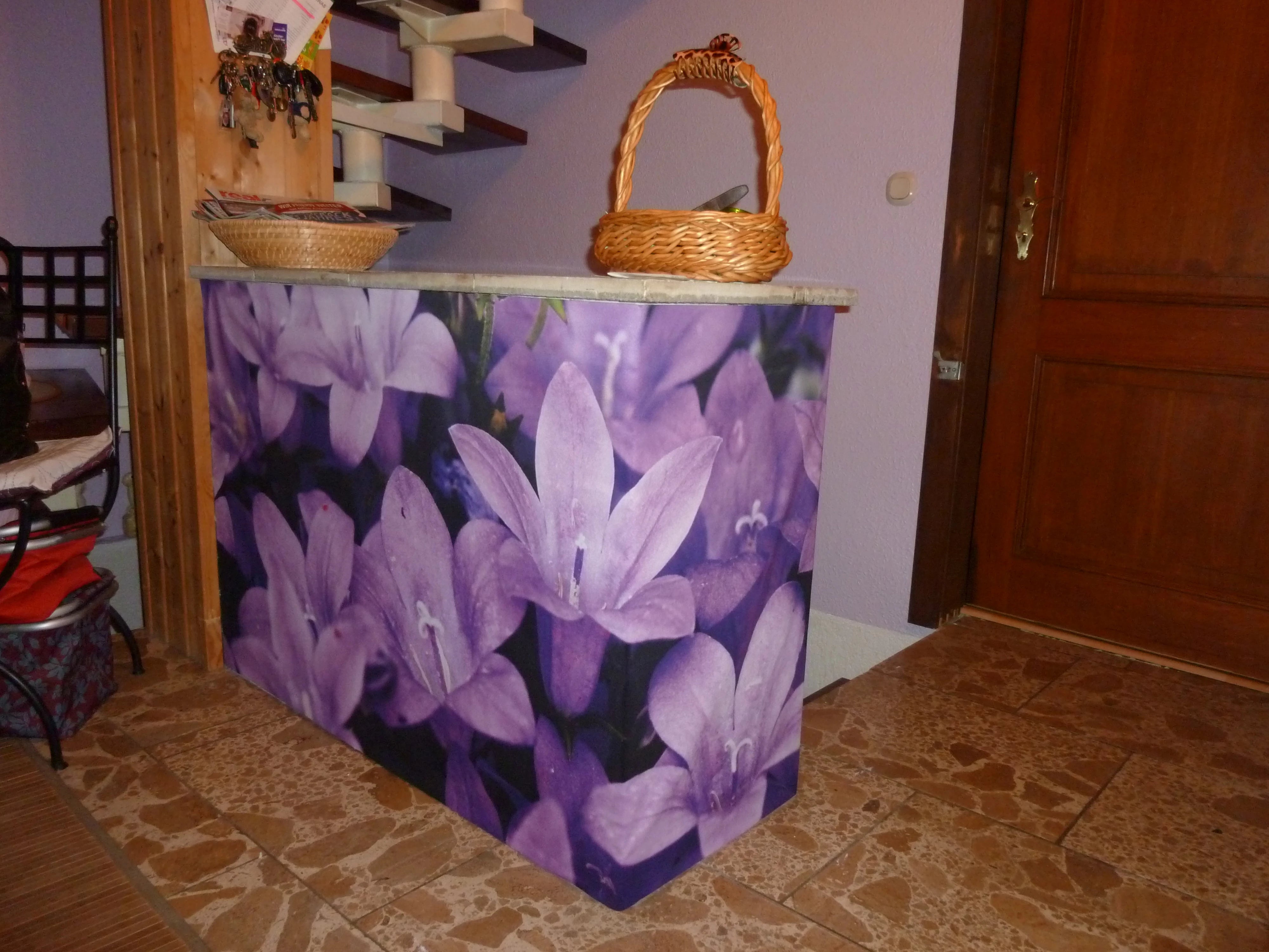 Ein Tresen im Hausflur wird mit einem mit Glockenblumen lila Blumen bedruckten Stoff verhüllt