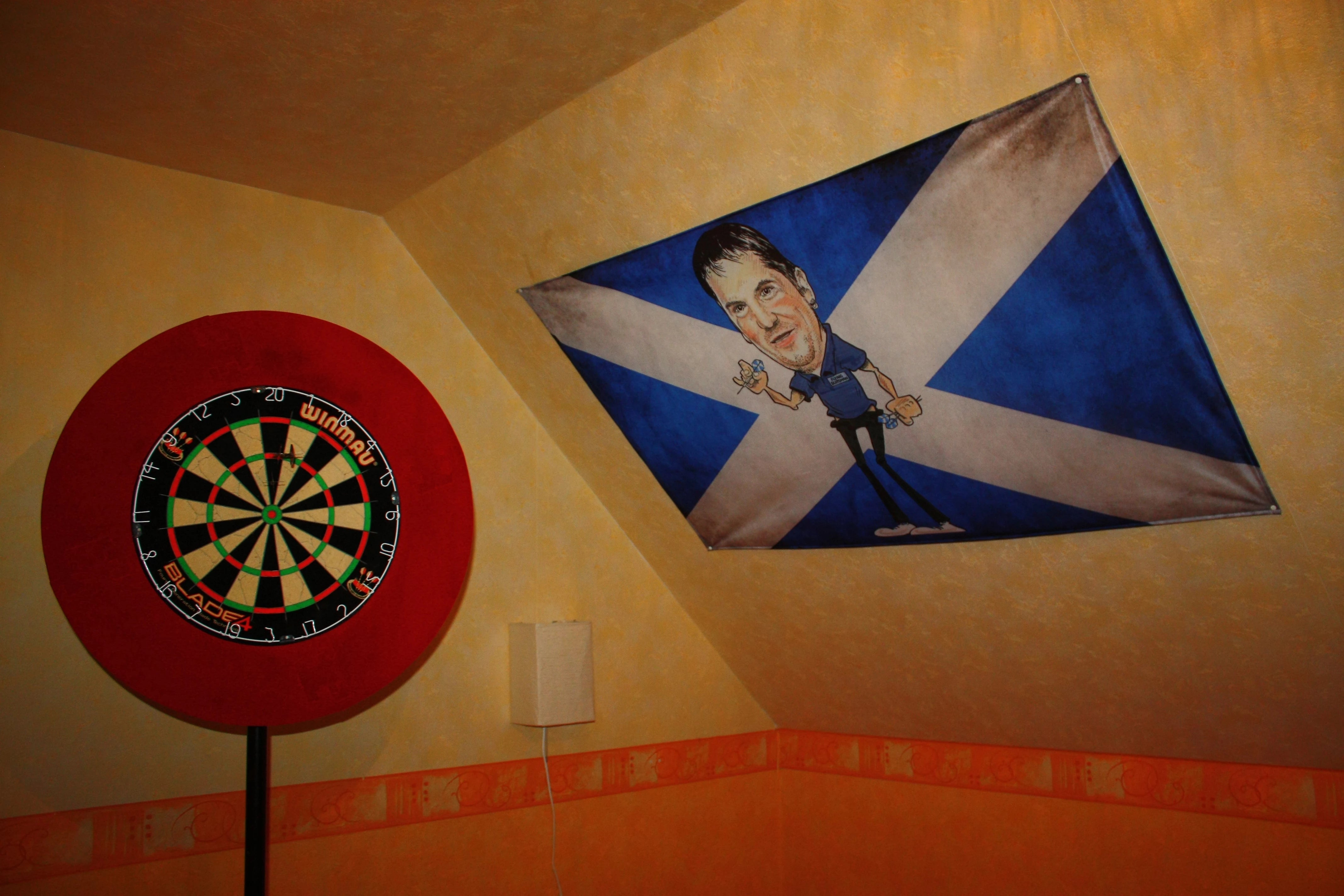 mit Karikatur des Darts-Spieler Gary Anderson bedruckte Foto-Fahne an der Dachschräge neben der Dart-Scheibe im Schlafzimmer 