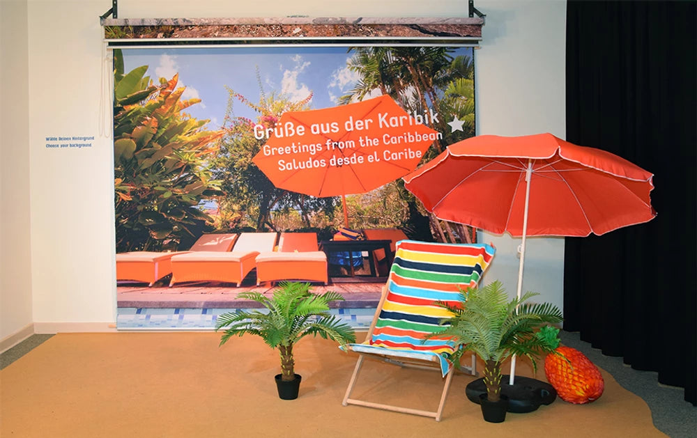 Fotorollo als Fotohintergrund bedruckt mit Grüßen aus der Karibik einer Ausstellung im botanischen Garten in Berlin mit Liegestuhl, Palme und Sonnenschirm für Besucher, um sich fotografieren zu lassen 