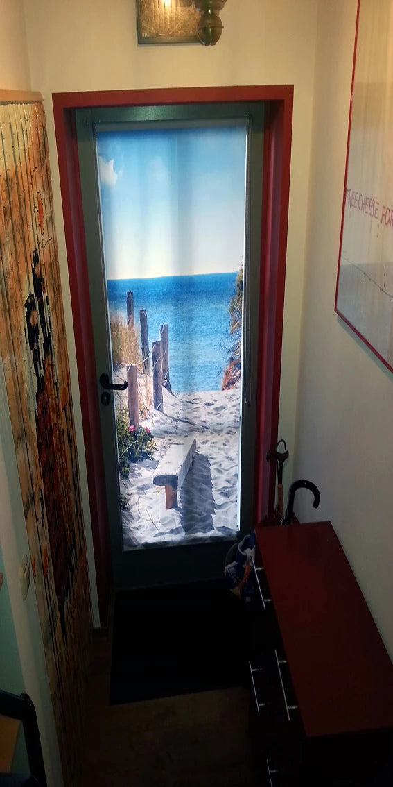 Die Haustür aus Glas wird zum Sichtschutz verdeckt mit einem Fotorollo mit gedrucktem Strandmotiv auf dem eine Düne und das Meer zu sehen sind