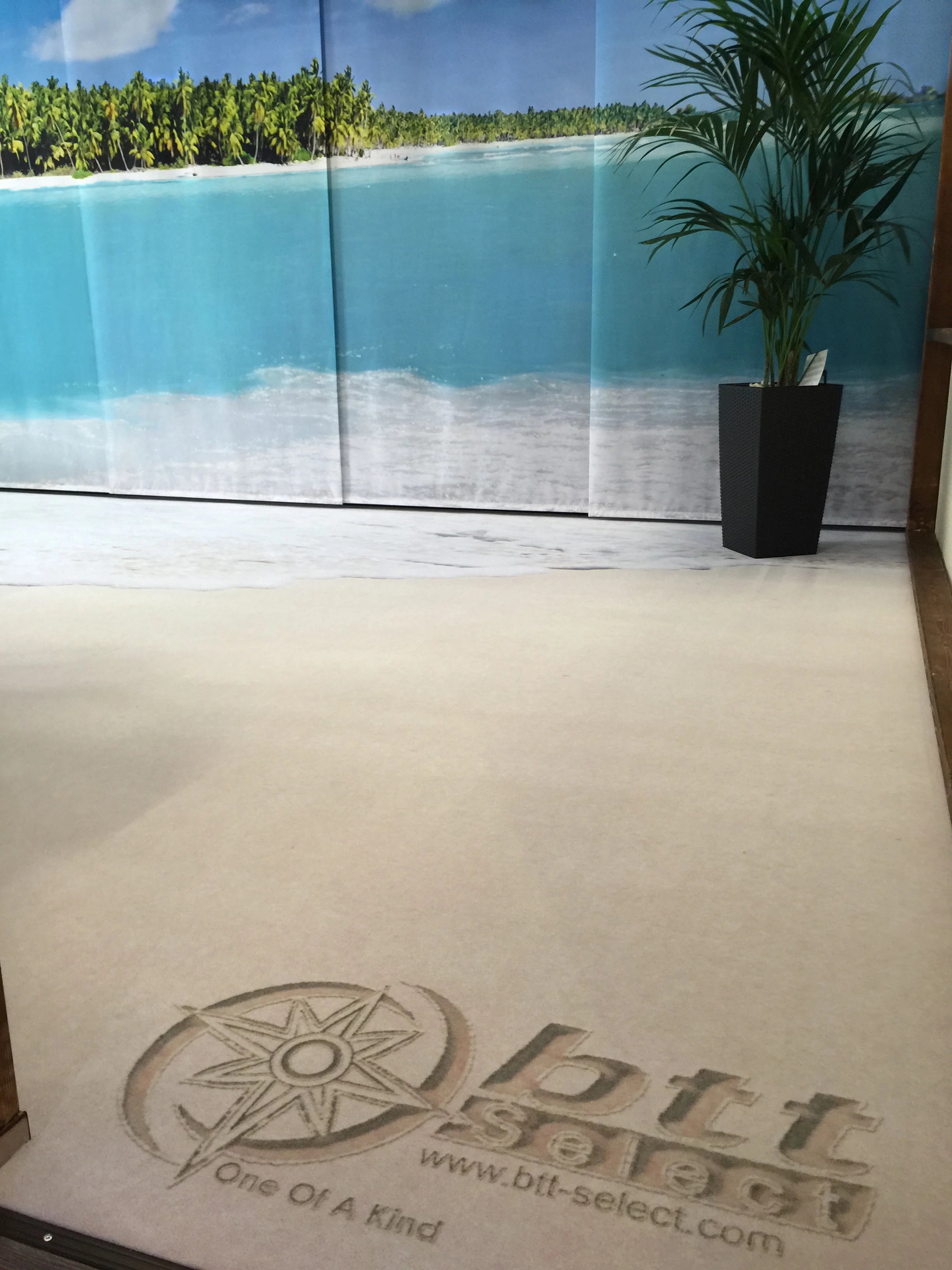 Fototeppich mit Logo des Reisebüros bedruckt das aussieht als ob jemand das Logo in den Sand gemalt hat