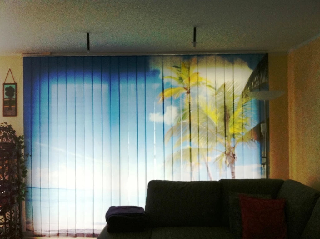 Im Wohnzimmer hängt ein mit Palme und Meer bedruckter auf Maß gefertigter Lamellenvorhang am Fenster